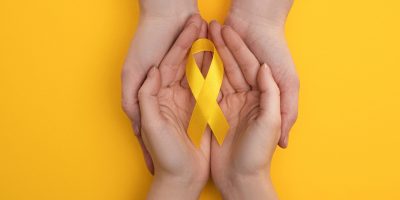 Cropped view of couple holding yellow ribbon on colorful background, international childhood cancer