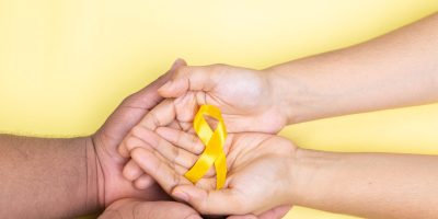two hands holding yellow ribbon, childhood cancer, yellow background