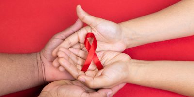 two hands holding red ribbon, acquired immunodeficiency syndrome, red background